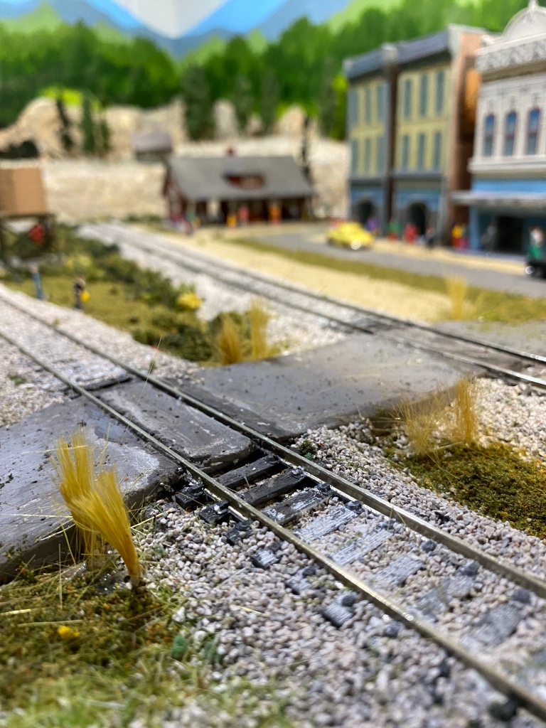 Two HO scale tracks, ballast, weeds, buildings, cars, train station