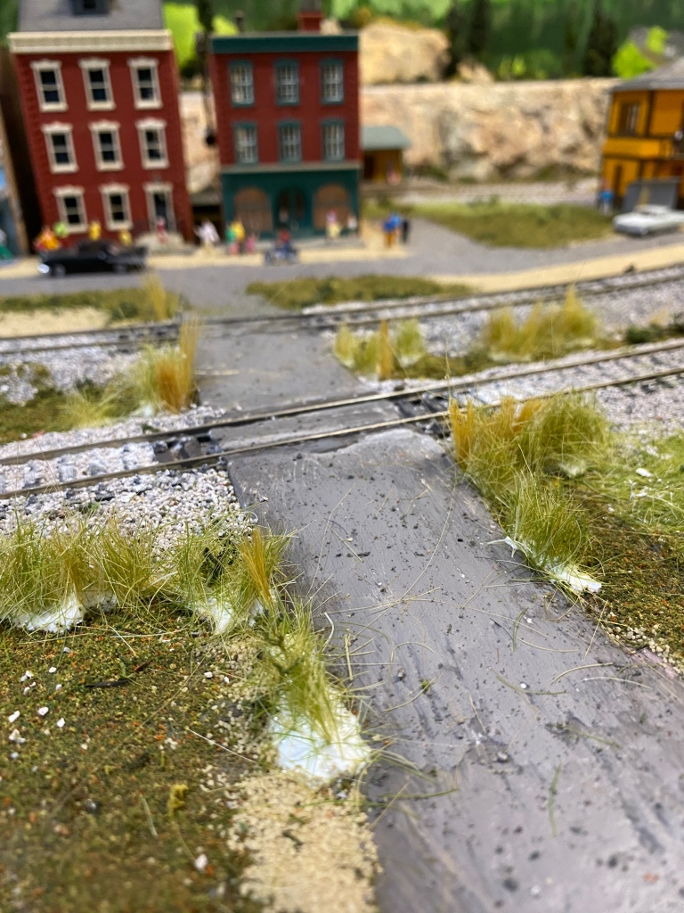 Buildings, railroad crossing, weeds growing near road, train tracks