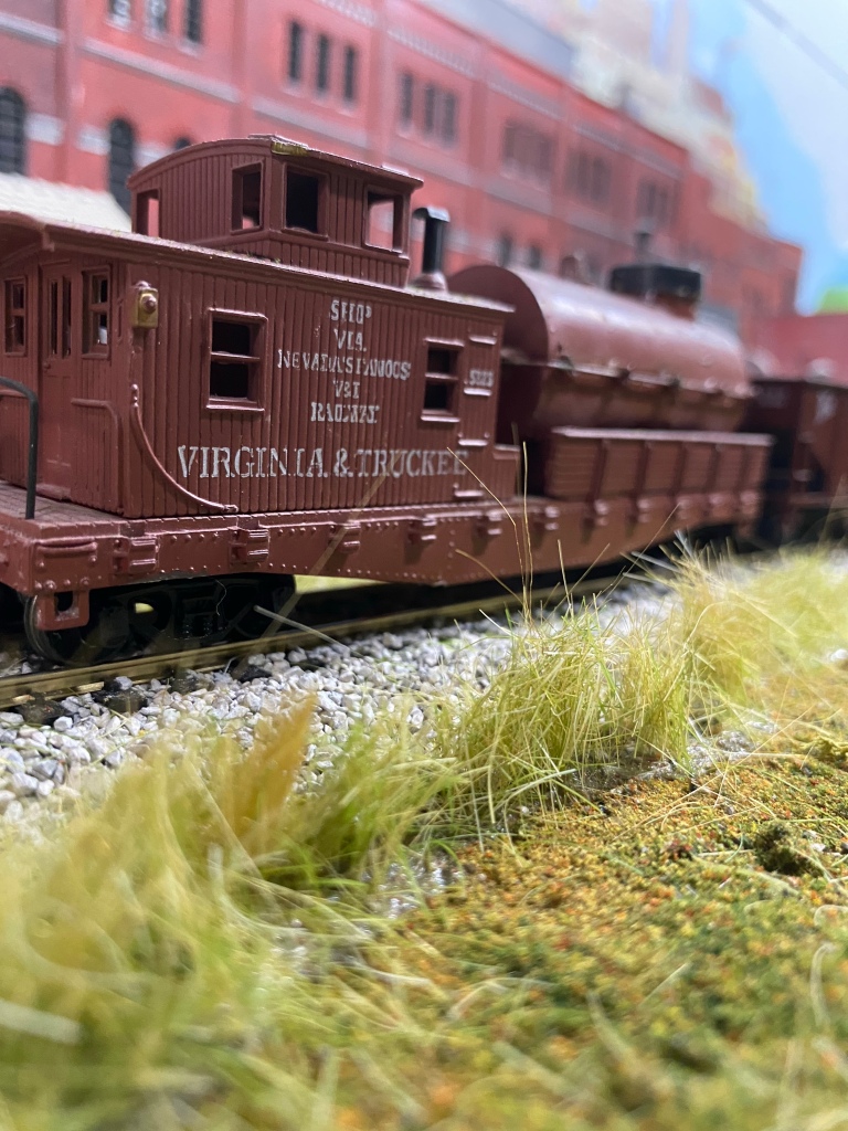 HO scale caboose, weeds, a factory, grass, track